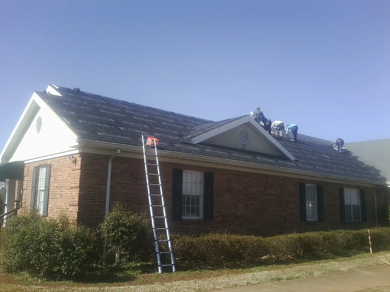 Crew tearing shingles off a brick ranch roof with a ladder set — Emergency Roof Repair work by our crew in Sayreville