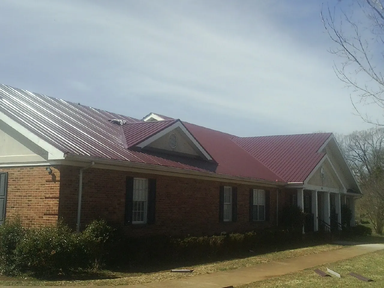 Red metal roof with gabled entries on a long brick building, from a Hail Damage Roof Repair job in Sayreville