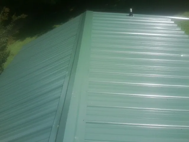 New green metal panels meeting at the ridge of a roof — Flat Roof Repair work by our crew in Sayreville