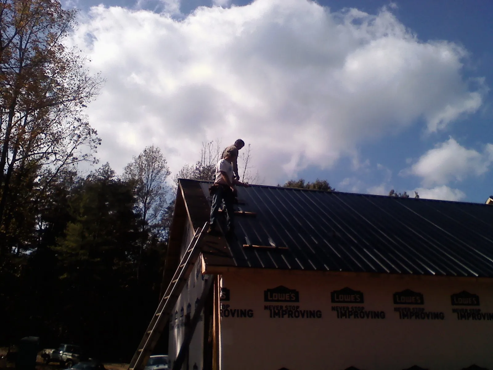 Roofer fastening dark metal panels high against a cloudy sky, from a Roof Inspection job in Sayreville