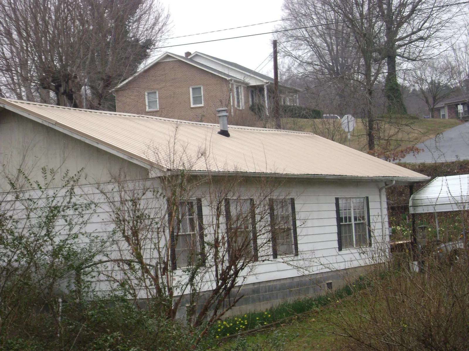 Tan metal roof on a white sided house set into a hillside — Commercial Roofing by Roofing Brothers in Sayreville